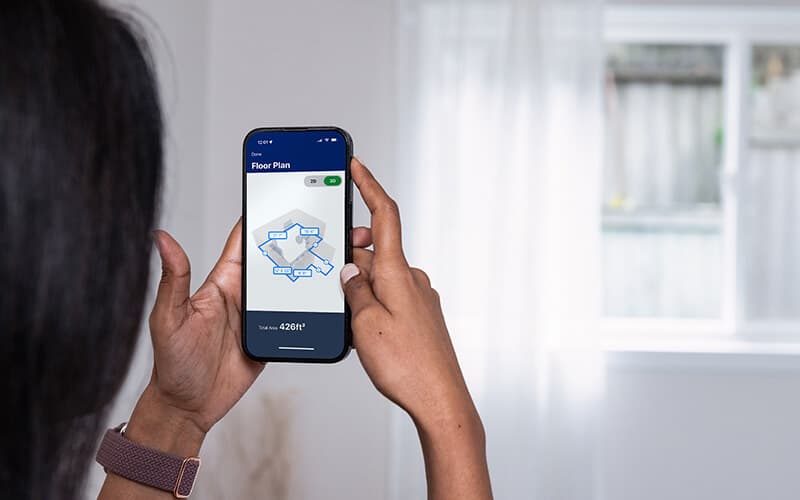 Hands holding a phone that displays a measured floor plan.